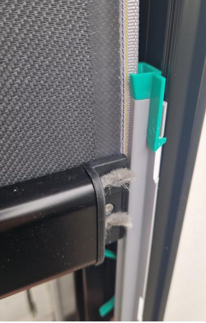 Nærbilde av en sideskinne der PVC-skinnen med grønne/turkise låseklips holder screendukens kant fast
