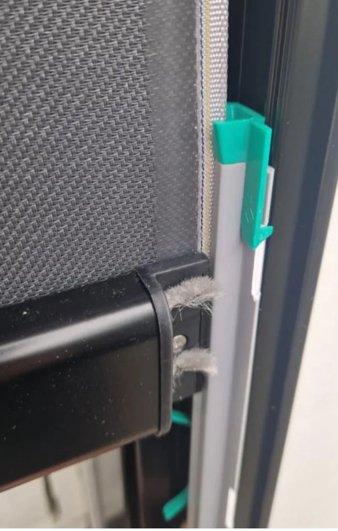 Nærbilde av en sideskinne der PVC-skinnen med grønne/turkise låseklips holder screendukens kant fast