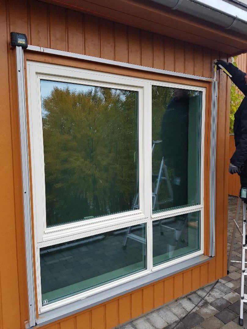 Fotografi av et vindu der sideskinnene er festet først på fasaden, sett skrått forfra